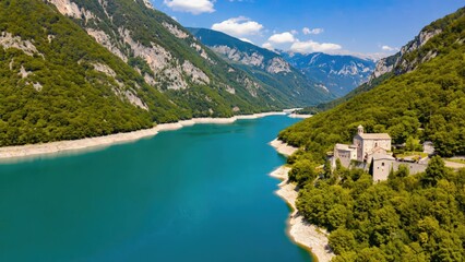 Fototapeta premium Stunning turquoise reservoir lake surrounded by lush green mountains and a historic medieval castle in the Alps, Italy.