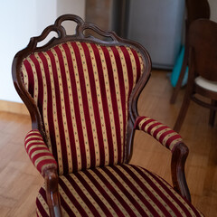 Antique wooden armchair upholstered in a red and gold striped fabric stands on a wooden floor © Denis Renkas