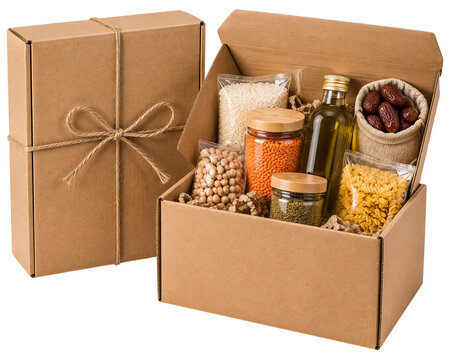 Cardboard gift box filled with assorted dry food staples, glass jars, and a bottle of olive oil isolated on a transparent background
