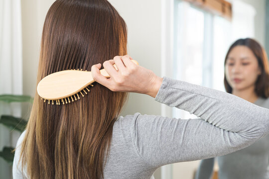 Health hair care, beauty concept. Asian woman hand holding hairbrush and brushing, girl combing long straight hair in morning routine after wash and treatment at home.