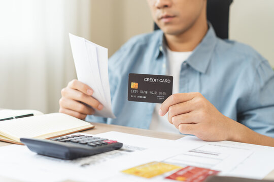 Asian young man holding credit card and bills while using a calculator to calculate monthly expenses, financial planning, debt management and personal budget concept.