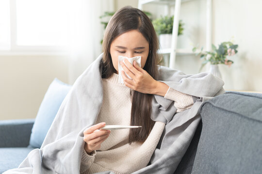 Sick, influenza asian young woman tired have a fever and sore cough hand holding thermometer for check measure body temperature, illness while rest at home. Health care with disease, pandemic virus.