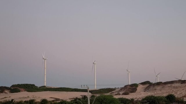 Wind farm turbines on coastal sand dunes at sunset, Canoa Quebrada Brazil