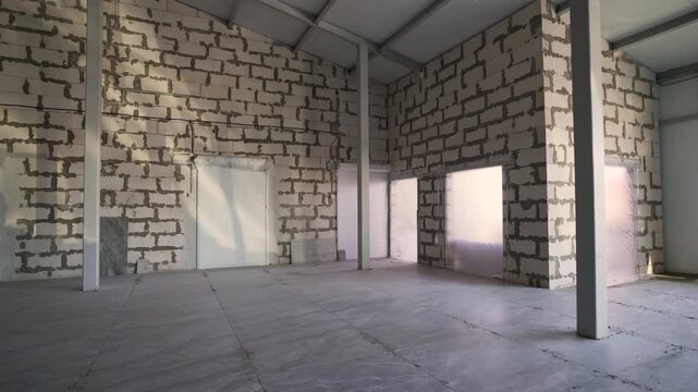 Interior of a large, empty commercial building during renovation. The walls are made of concrete blocks and the floor is tiled. Slow camera movement reveals the spacious, unfinished room