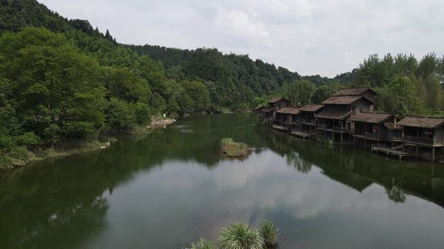 Traditional wooden stilt houses beside a calm green lake surrounded by lush forest