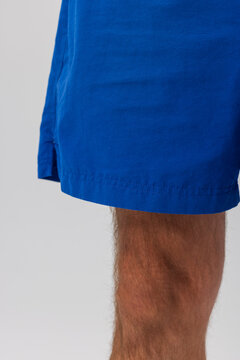 Close-up of a blue garment hem with visible stitching, showing a leg with hair. Minimalist studio shot, clean background.
