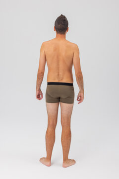 Full-body rear view portrait of a shirtless man wearing olive green boxer briefs, standing barefoot against a clean light studio background. Ideal for underwear mockups and fitness stock.