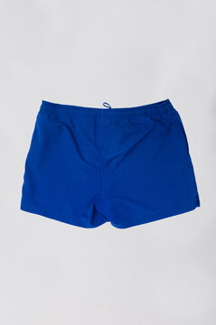 Classic blue men's swim trunks isolated on white background. Casual summer beachwear, board shorts with elastic waistband, perfect for swimming, pool, watersports, and active tropical vacations.