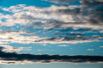 Horizontal bands of dark stratocumulus and sunlit altocumulus clouds drift across a bright azure sky during late afternoon. © Andrey