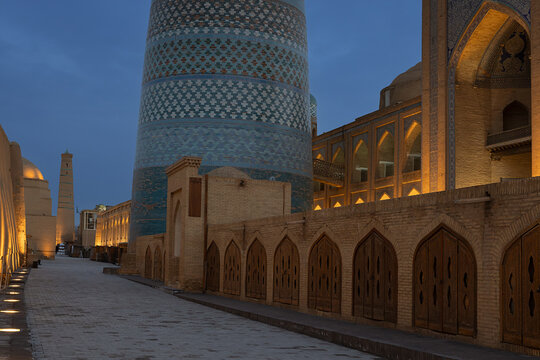 Kalta Minor minaret in Ichan Kala at blue hour with illuminated historic buildings along an empty street in Khiva, Uzbekistan. Ideal for travel publications, heritage brochures, and tourism marketing.