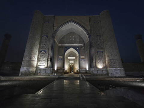 Bibi Khanym Mosque illuminated at night in Samarkand, Uzbekistan, with intricate geometric carvings on the massive portal facade. Ideal for travel publications, heritage projects, and cultural.