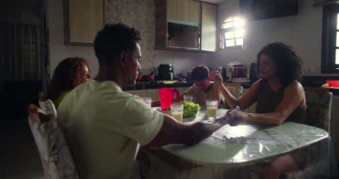 Family holding hands in prayer before dinner at the dining table, emphasizing spirituality, faith, gratitude, and unity in a peaceful home environment