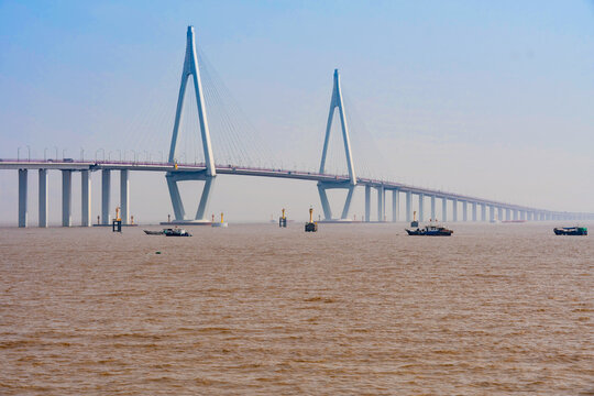 Cable-stayed bridge spanning a wide muddy river with small boats passing beneath