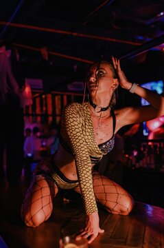 Go-go dancer performs on a nightclub bar in fishnet stagewear under dramatic red and blue neon lights, capturing energetic club entertainment for nightlife and party event promotion