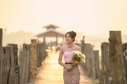 Portrait of a smiling Burmese woman walking across U Bein Bridge carrying a bunch of flowers at sunrise, Mandalay, Myanmar