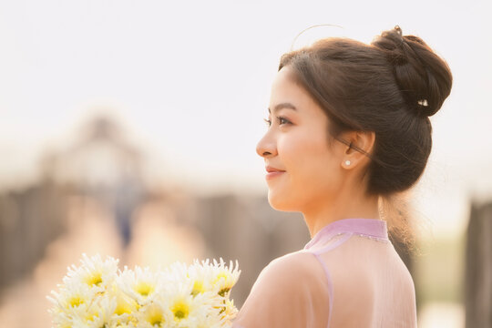 Side view of a smiling Burmese woman standing on U Bein Bridge carrying a bunch of flowers at sunrise, Mandalay, Myanmar