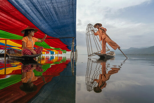 Split screen of a Traditional Fisherman with a cone fishing trap standing on a boat and a Local Weaver sitting in a Wooden Boat under a Colourful lotus silk Canopy, Inle Lake, Shan State, Myanmar