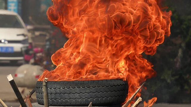 Burning Tire With Large Orange Flames And Black Smoke On Urban Street