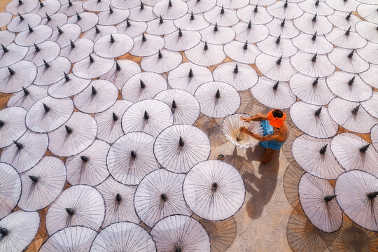 Overhead view of a senior shirtless man arranging traditional oiled paper umbrellas (Pathein Htee) in the sun to dry, Mandalay, Myanmar