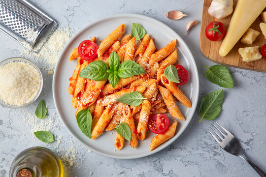 Classic italian pasta penne alla arrabiata with basil and freshly grated parmesan cheese on dark table. Penne pasta with chili sauce arrabbiata.