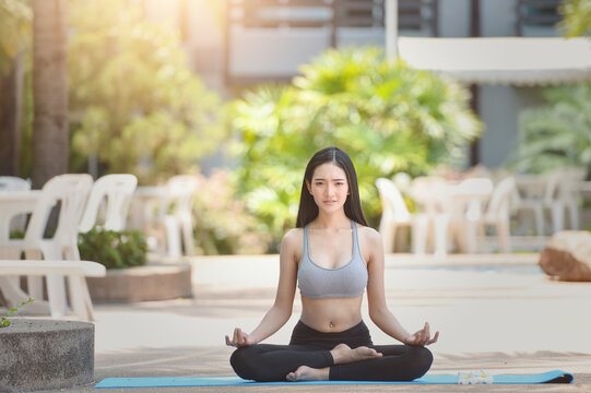 Young woman in sportswear sitting outdoors in a cross-legged lotus yoga pose (Padmasana) with her hands in a chin mudra pose practicing mindful meditation at an outdoor resort