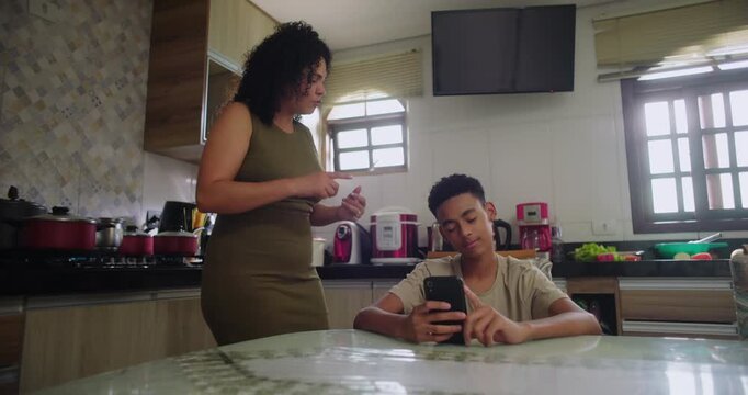 Mother firmly taking phone from teenage son during heated moment, addressing screen time and technology boundaries, highlighting family conflict and parenting challenges