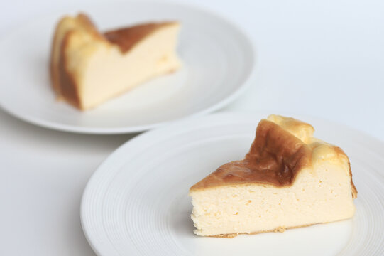 Close-up of two plates with slices of Basque cheesecake on a white background