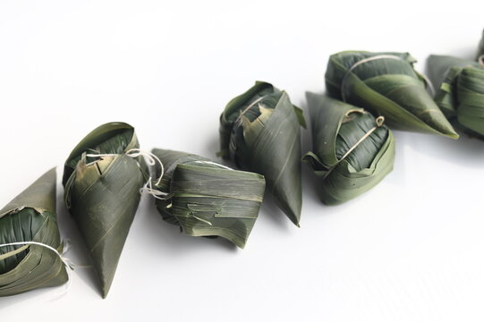 Close-up of a row of traditional rice dumplings wrapped in bamboo leaves (Zongzi) on a white background