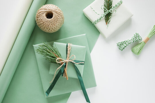 Overhead view of wrapped gifts, wrapping paper, a ball of string and roll of wrapping paper on a white background