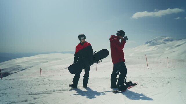 Two snowboarders prepare their equipment on a sunny winter mountain. Friends stand on a snowy slope, getting ready for an exciting day of snowboarding.