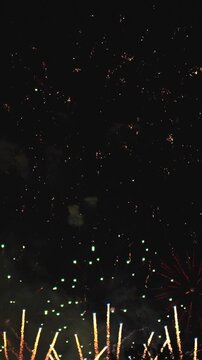 VERTICAL VIDEO: Golden Fireworks Bursting Against Dark Night Sky With Elegant Spark Trails. Festive Background For New Year, Christmas, Holiday And Celebration.
