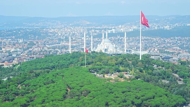 Aerial view of a green hill with Turkish flag and cityscape in the background, showcasing residential areas and urban development in Istanbul, Turkey 