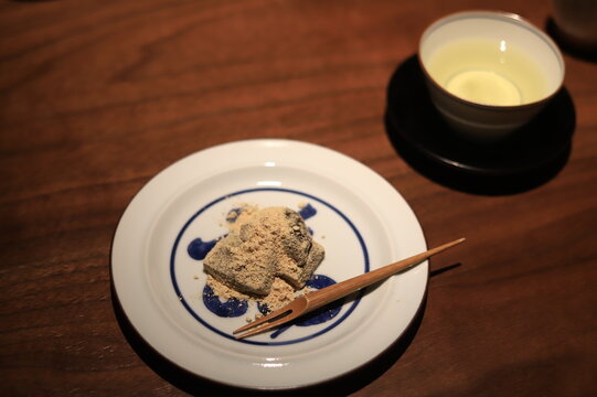 Close-up of brown sugar flavoured bracken starch dumplings (warabi mochi) with a cup of green tea on a table