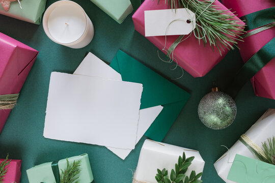 Overhead view of a blank card, envelopes and wrapped Christmas gifts decorated with festive foliage on a table with a block candle and Christmas bauble