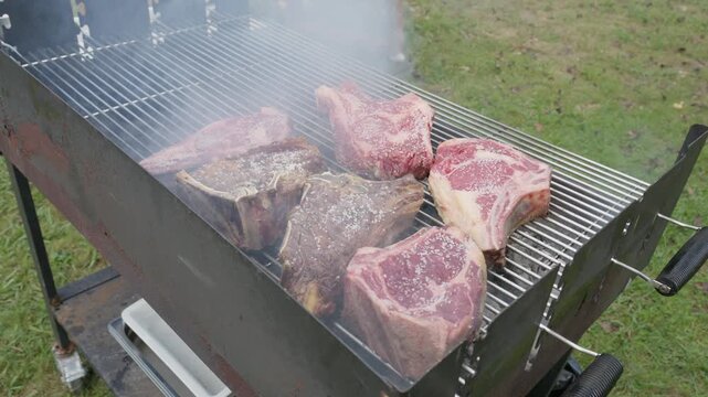 High angle view of tomahawk and t-bone steaks cooking on a large outdoor barbecue grill