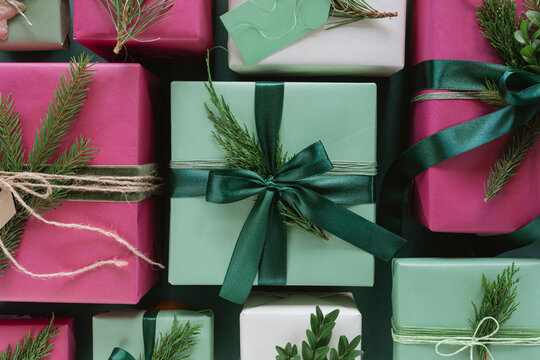 Overhead view of assorted wrapped Christmas gift boxes decorated with blank gift tags, evergreen sprigs, velvet ribbon and pinecones