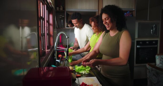 Mother cutting vegetables, father washing lettuce, teenage daughter helping in kitchen, family engaged in teamwork and bonding through shared meal preparation task