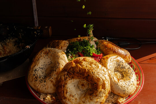 Close-up of fresh herbs being sprinkled on a tandoor bread and pilaf platter