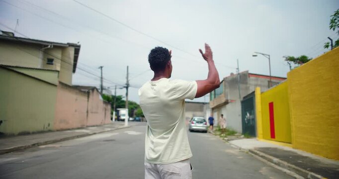 Man of African descent standing in an urban street, raising arms toward the sky, expressing gratitude and faith, symbolizing spiritual connection and hope