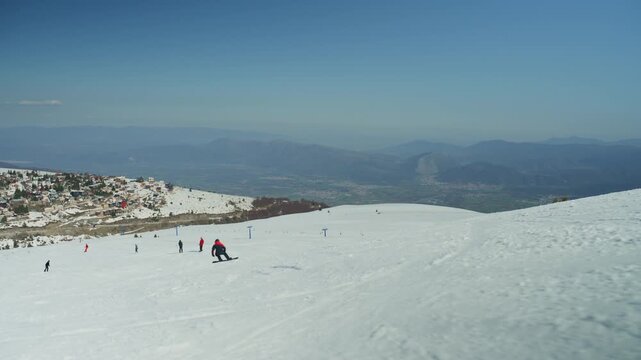 Snowboarders and skiers enjoy a sunny day on a snow-covered mountain slope. The popular winter resort offers scenic views of the alpine village and distant peaks.