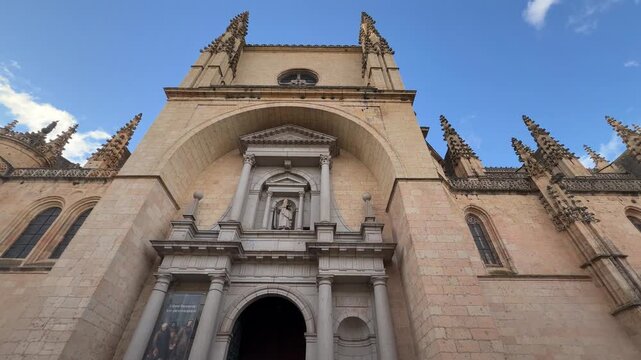 Low angle architectural shot revealing the monumental stone facade, ornate Gothic spires, and intricate portal of the historic Segovia Cathedral on a sunny winter day in Spain.