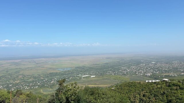 Panoramic landscape featuring green hills and a vast valley under a bright blue sky, highlighting the natural beauty of the mountainous area