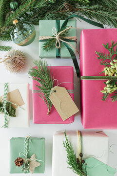 Overhead view of assorted wrapped Christmas gifts decorated with blank gift tags, evergreen sprigs, velvet ribbon, pinecones, Christmas baubles and ornaments on a beige background