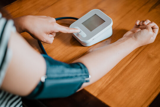 High-angle photo of a woman pressing the start button on a digital blood pressure monitor with a cuff on her arm. Healthcare checking concept.
