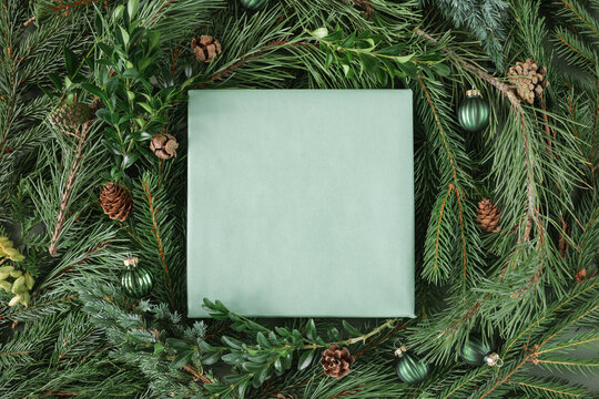 Overhead view of a blank card framed by lush fir branches, pinecones and Christmas baubles