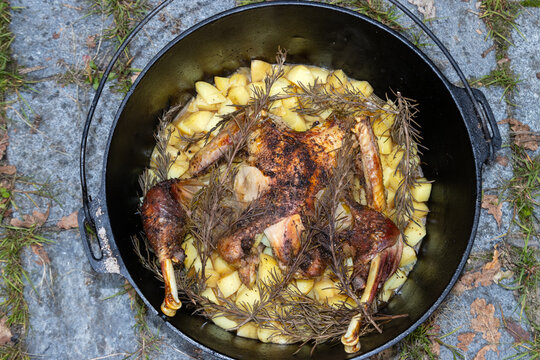 Crispy golden brown baked whole chicken with potatoes and rosemary in a pot.