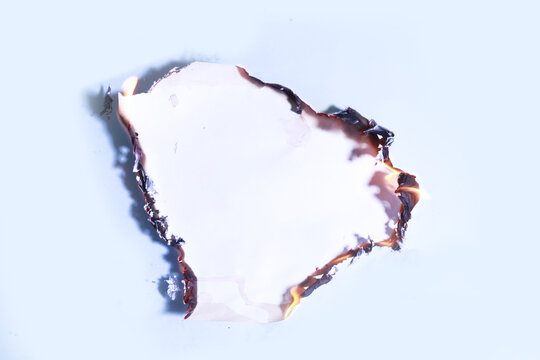 Burning edges of white paper sheet glowing with bright orange fire flames on blue background