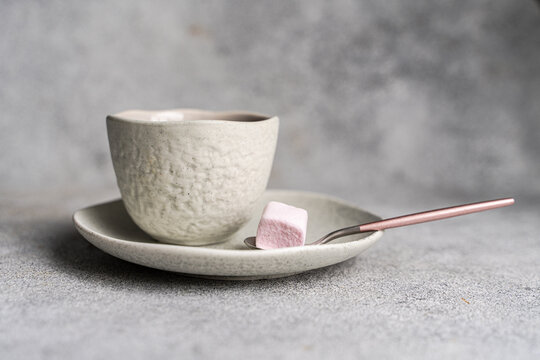 Close-up of a cup of black coffee with a pink marshmallow  on a grey concrete table