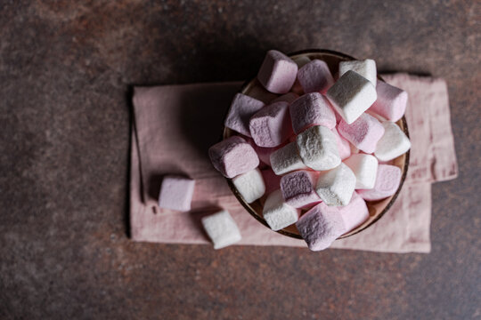 Overhead view of a bowl of pink and white marshmallows on a napkin and concrete table