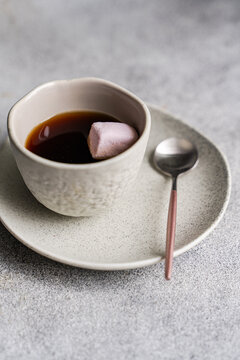 Close-up of a cup of black coffee with a pink marshmallow on a grey concrete table